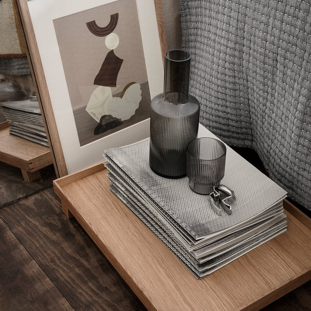 "Gray textured patterns on table with dark glass vase and cup, featuring abstract art and natural wood elements."