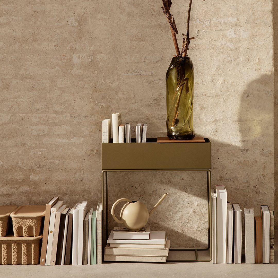 Green and beige storage table with a sleek design, paired with a textured vase and stacked books against a neutral backdrop.