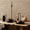 Elegant black dinnerware and candle holder on a rustic wooden table with soft beige textures and natural accents.