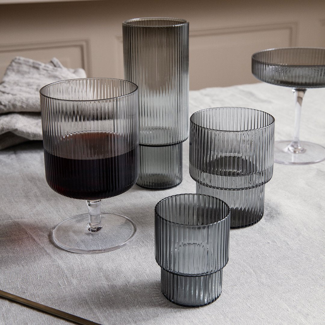 Set of ribbed gray glasses with varying heights and shapes, showcasing a modern and elegant design on a textured surface.