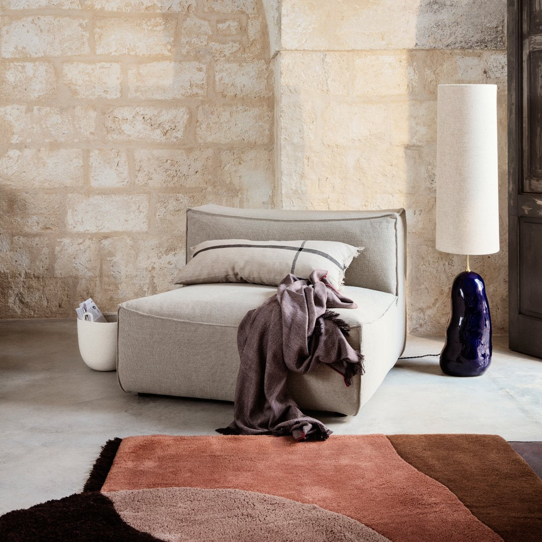 Light gray sofa with a textured fabric, accented by a dark purple vase and a rust-toned abstract patterned rug.