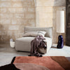 Light gray sofa with a textured fabric, accented by a dark purple vase and a rust-toned abstract patterned rug.
