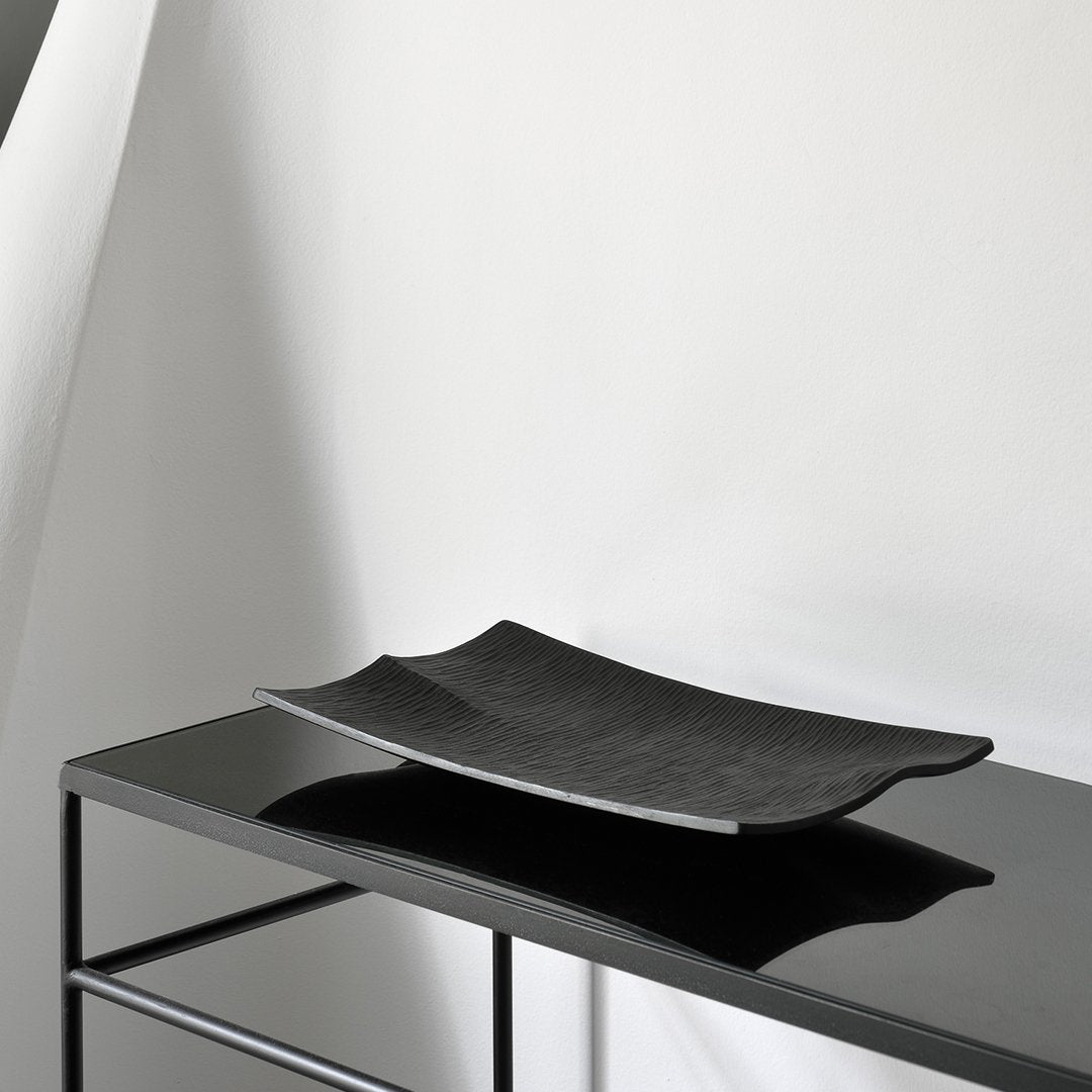 Black rectangular serving platter with a smooth, matte finish displayed on a sleek black surface.