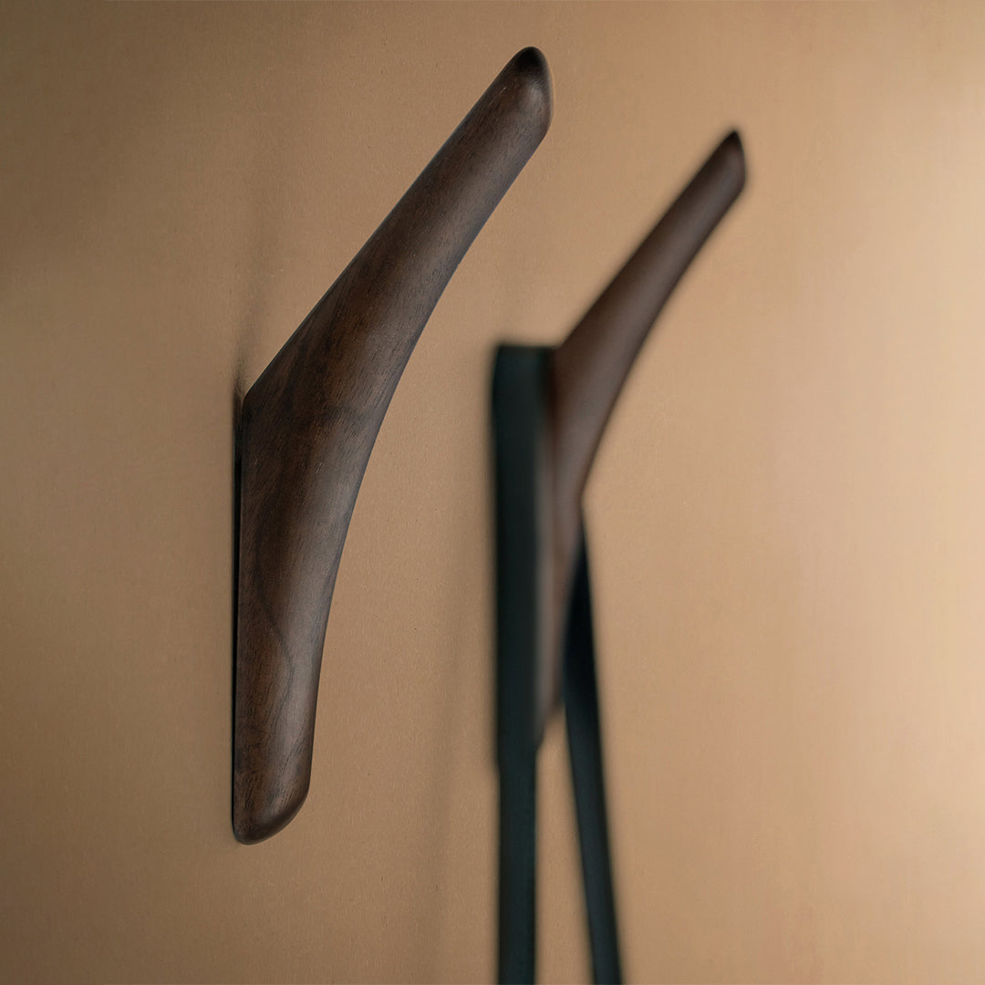 Dark wood wall hooks against a warm beige background, highlighting a smooth, minimalist design.