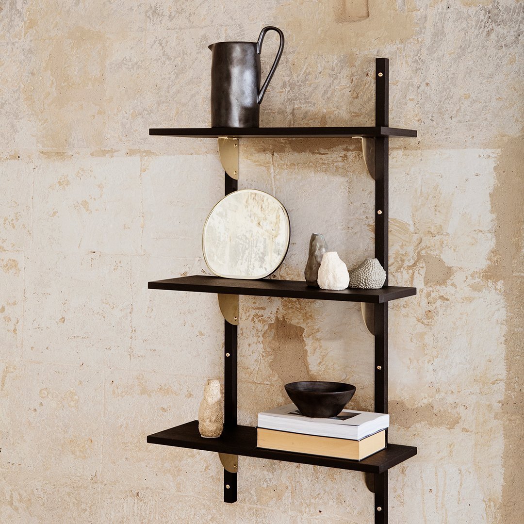 Black metal shelving unit against a textured beige wall, featuring minimalist decor items and a monochrome color palette.