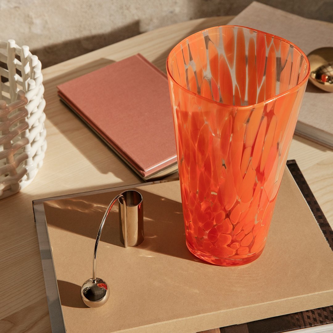 Vibrant orange glass vase with white and gold patterns, set on a wooden surface with pink and gold accents.