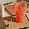 Vibrant orange glass vase with white and gold patterns, set on a wooden surface with pink and gold accents.