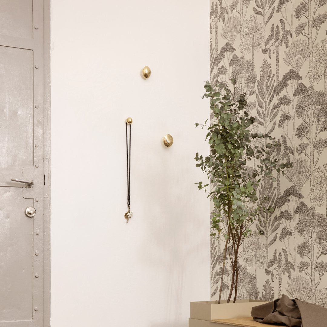 Brass wall hooks against a white wall, paired with a botanical patterned wallpaper in muted greys and greens.