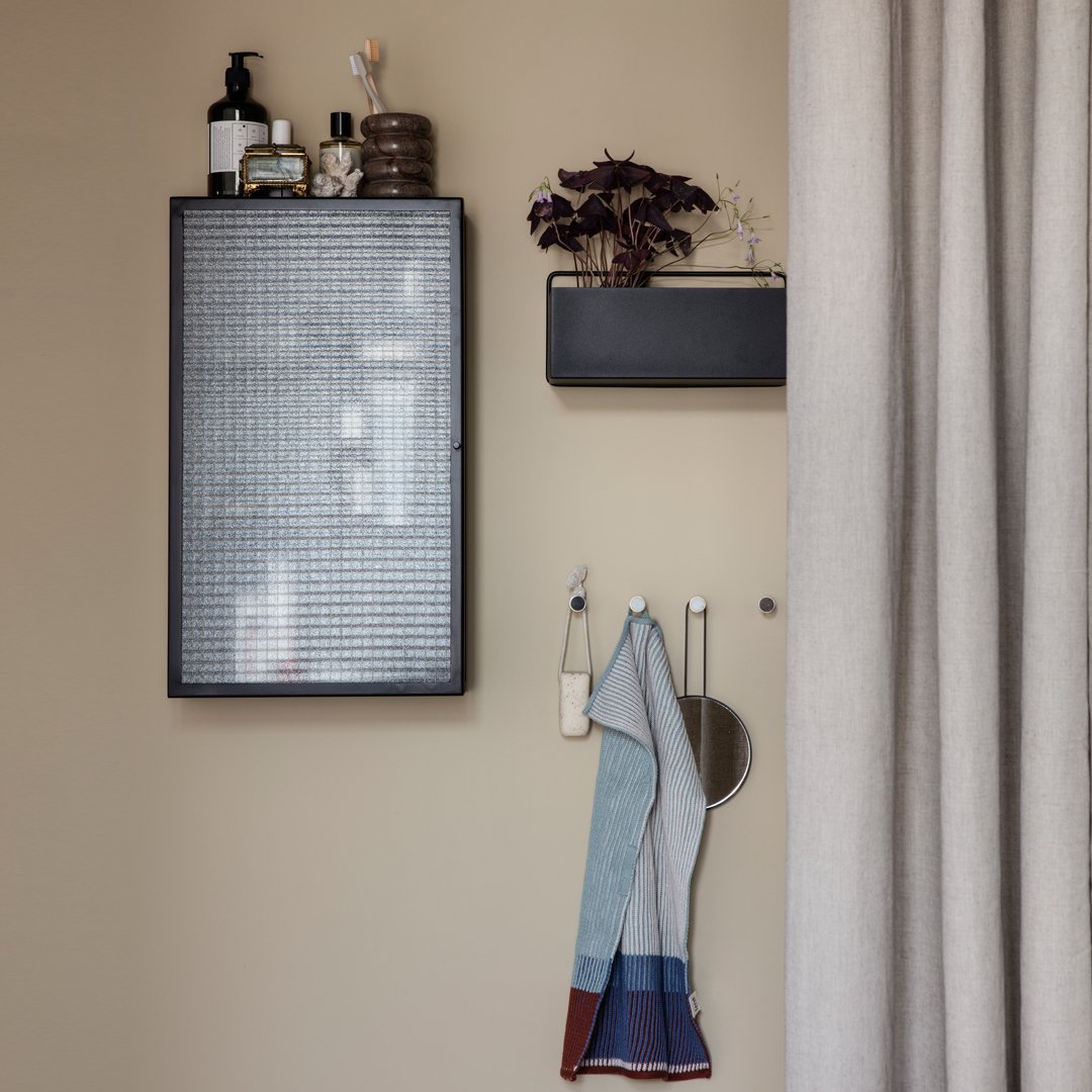 "Wall-mounted cabinet in black with a grid pattern; featuring a multicolored striped towel in soft blues and reds."