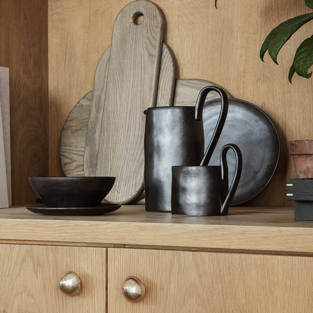 Black ceramic dinnerware set with a matte finish, featuring smooth curves and rustic wood accents.