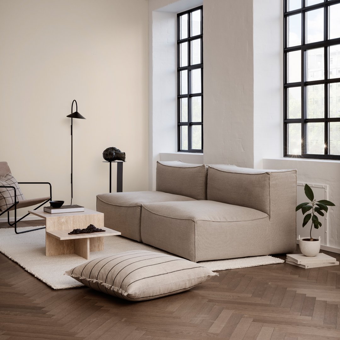Beige sectional sofa with textured fabric, paired with a light wood table and striped floor cushion in a modern, minimalistic setting.