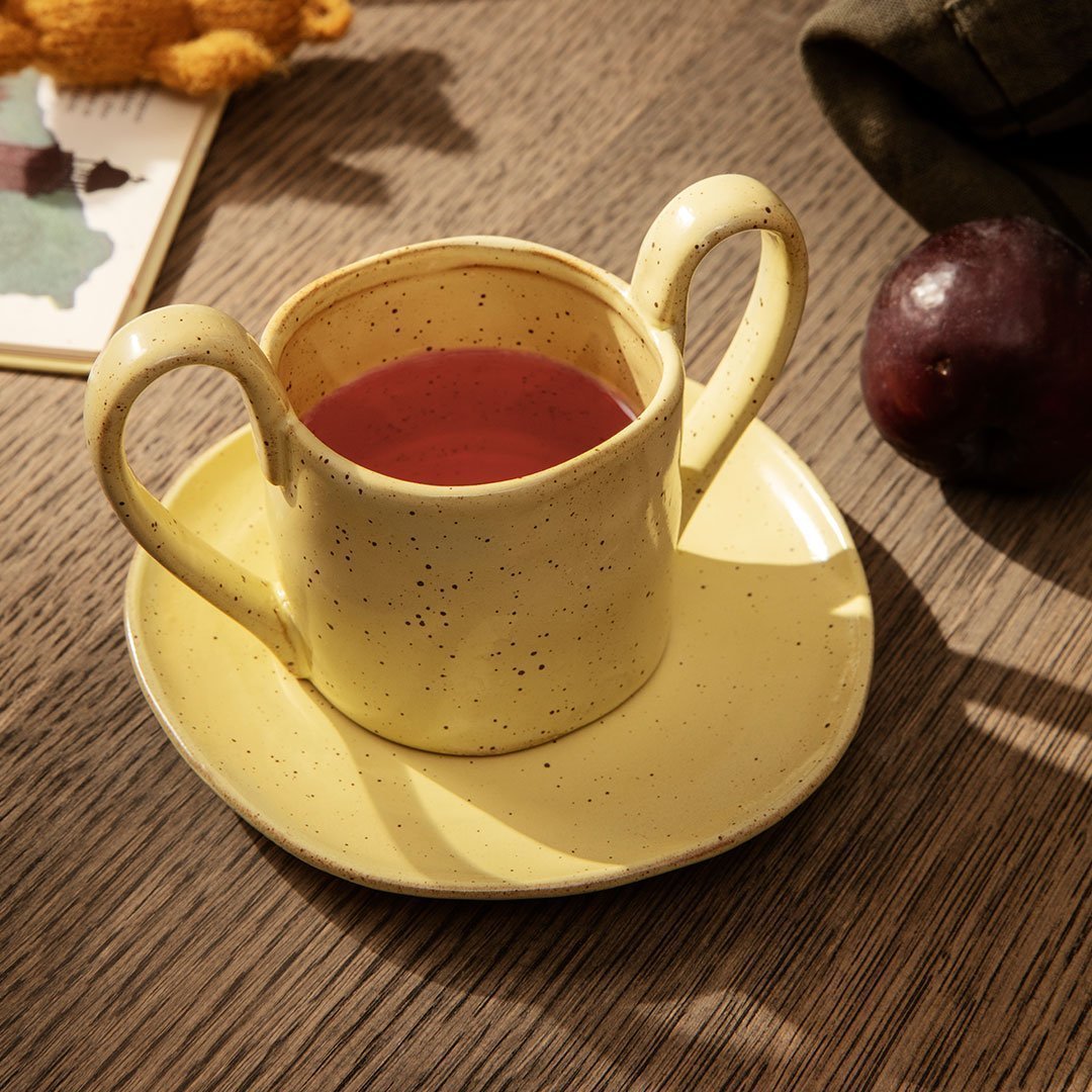 Ceramic cup and saucer in soft yellow with speckled texture, featuring a warm tea color.