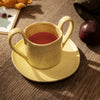Ceramic cup and saucer in soft yellow with speckled texture, featuring a warm tea color.