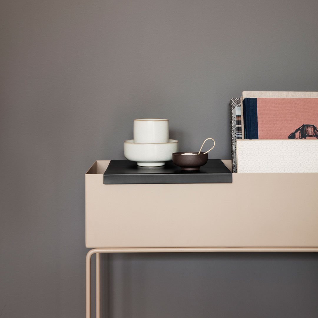 Modern beige console table with black tray, white and brown ceramics, and minimalistic book decor against a gray background.