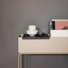 Modern beige console table with black tray, white and brown ceramics, and minimalistic book decor against a gray background.