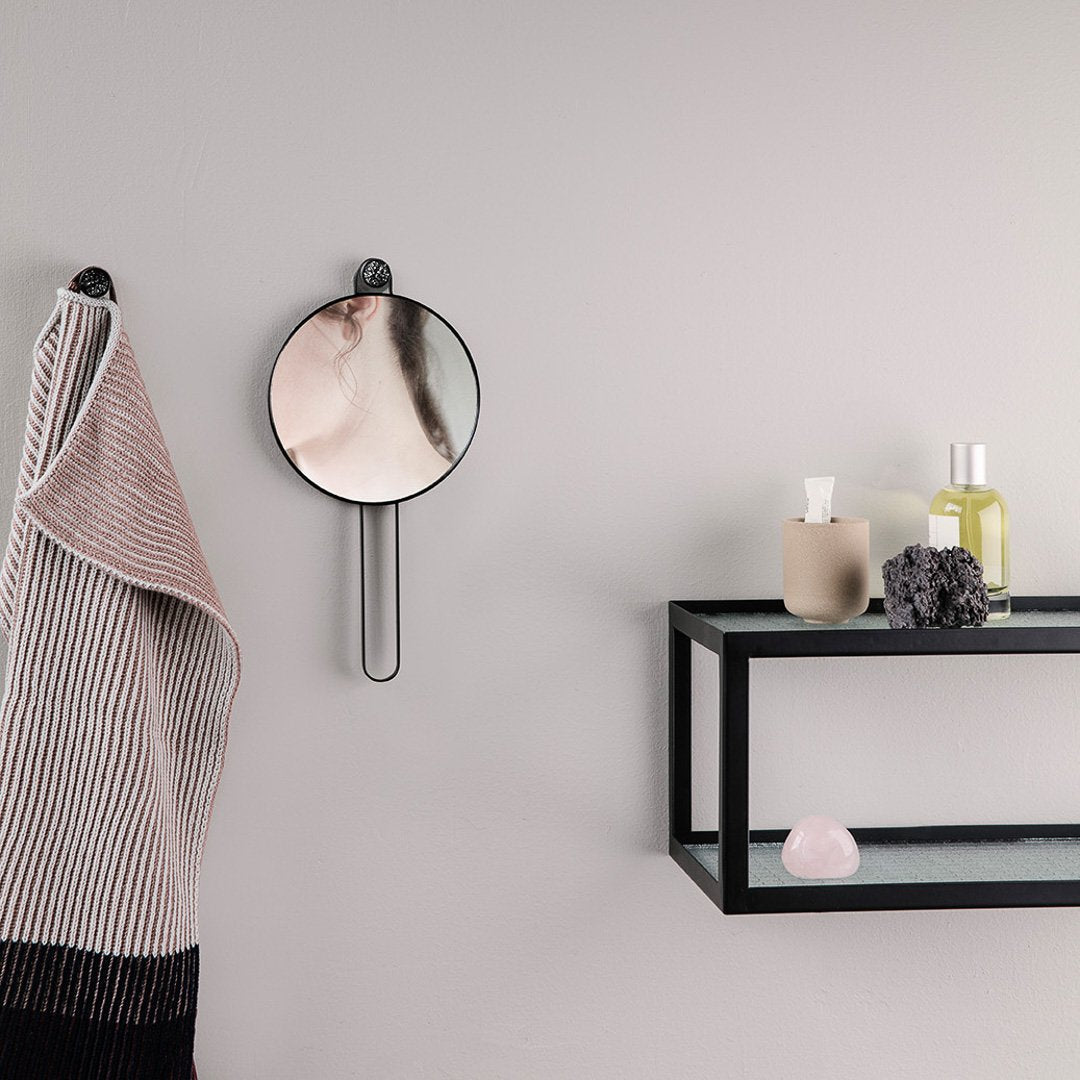Round mirror with a sleek black frame against a muted gray wall; stylish striped towel in soft pink and black. 