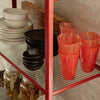 "Colorful glassware in vibrant orange and black, arranged on a red metal shelf with neutral dishware and jars."