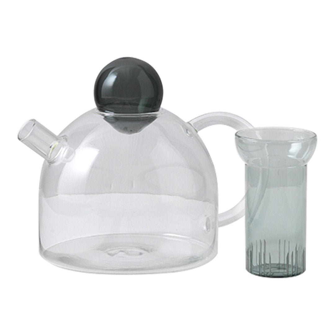 Clear glass teapot with a matte black lid and a textured green glass cup. Modern, minimalist design.