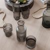 "Smoky gray glass vessels with vertical ribbed patterns on a light wooden surface."