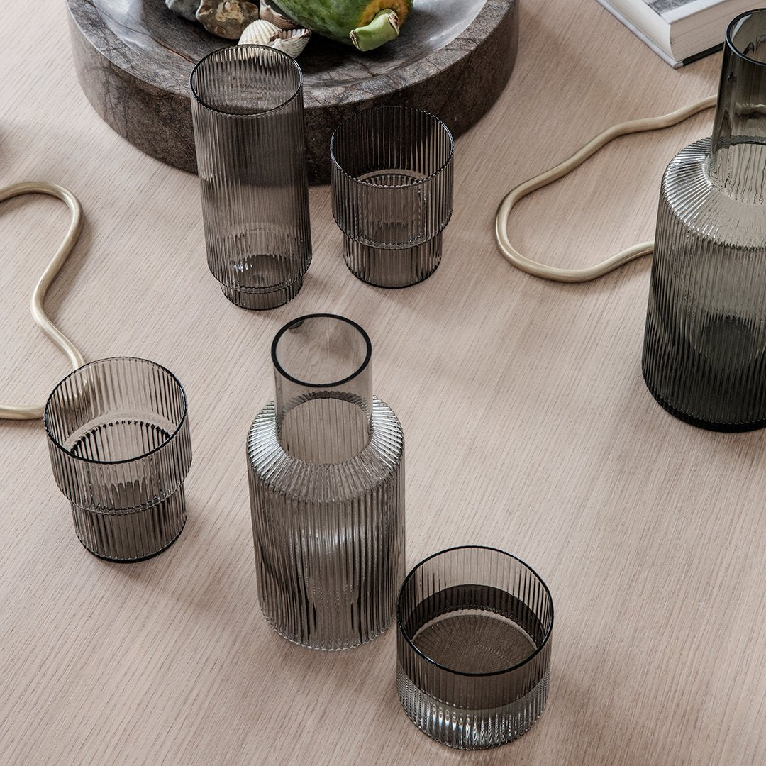 Set of sophisticated smoke-colored glass vases and cups with elegant ribbed patterns on a wooden surface.