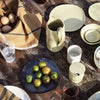 "Earthy tones with olive green, beige, and rich black; features a mix of smooth and textured dinnerware in rustic setting."
