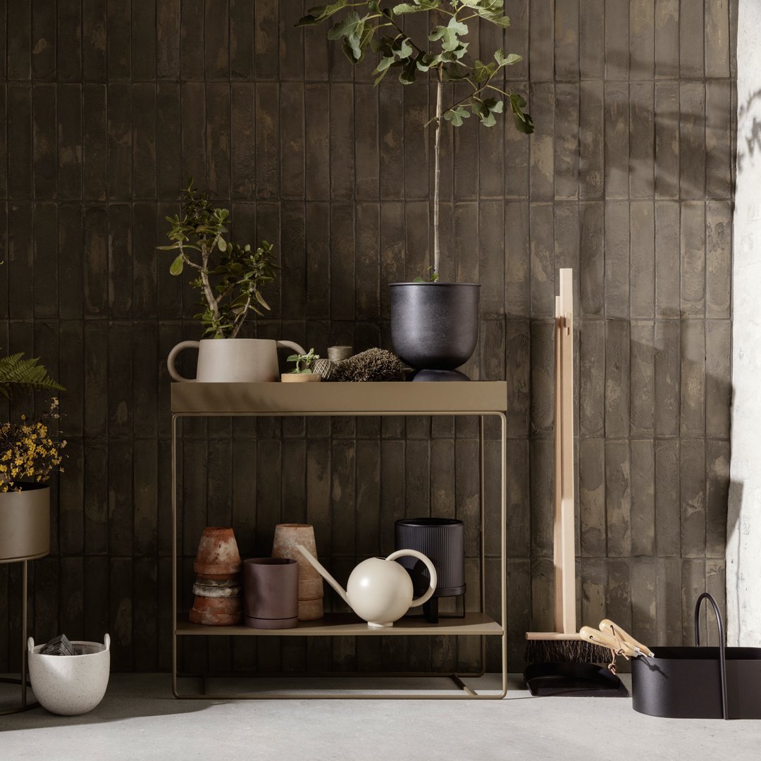 Stylish console table in earthy tones with neutral ceramics and greenery against a textured dark wall.