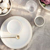 Elegant neutral dinnerware set featuring soft white tones and minimalistic design on a textured linen tablecloth.
