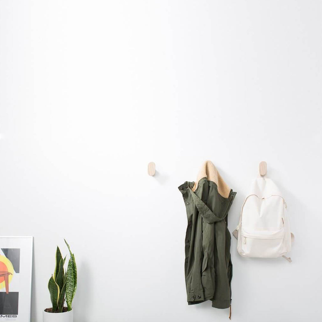 "Olive green jacket and white backpack hanging on minimalist hooks against a clean white wall."