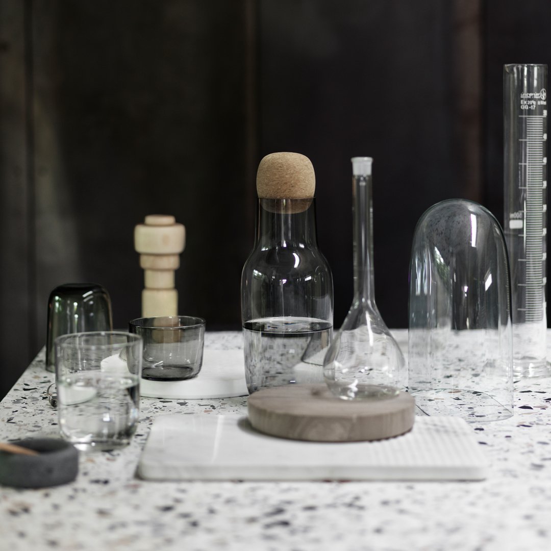 Clear glassware with cork and stone accents on a speckled white surface. Elegant, modern design aesthetic.