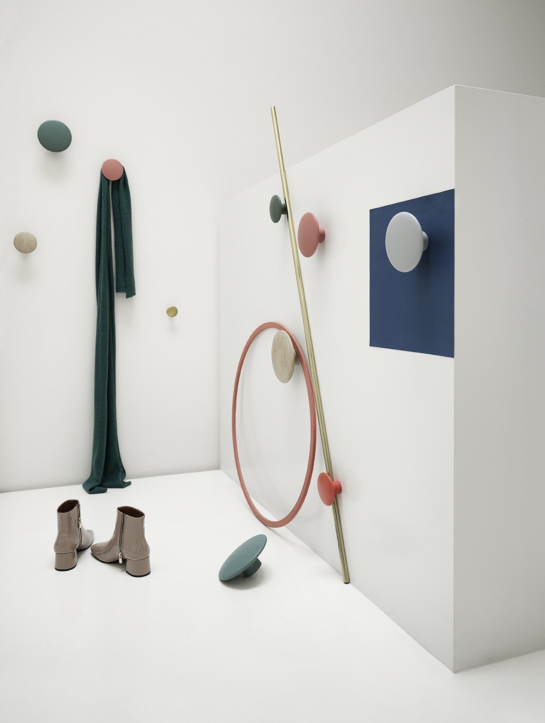 Colorful wall hooks in pastel shades, green drapery, and a blue accent panel against a minimalist white backdrop.
