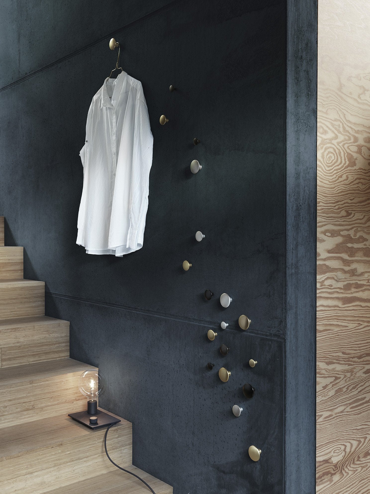 White shirt hanging on a dark textured wall, featuring varied metal hooks in gold, brass, and natural stone colors.