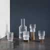 Elegant frosted glassware set with brass accents, featuring clear and matte textures against a dark background.