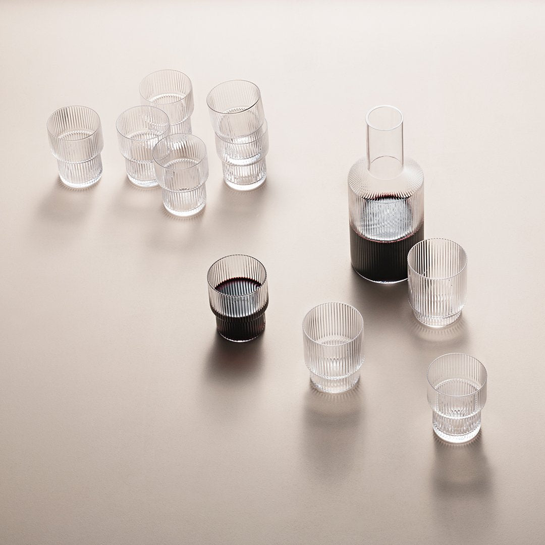 Clear glass drinkware set featuring a sleek carafe and various shot glasses with rich dark liquid.