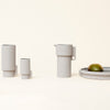 Gray ceramic pitcher and containers with minimalist design, set on a light background with a green lime accent.