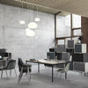 Modern office space featuring gray concrete walls, black and white furniture, and soft white pendant lighting.