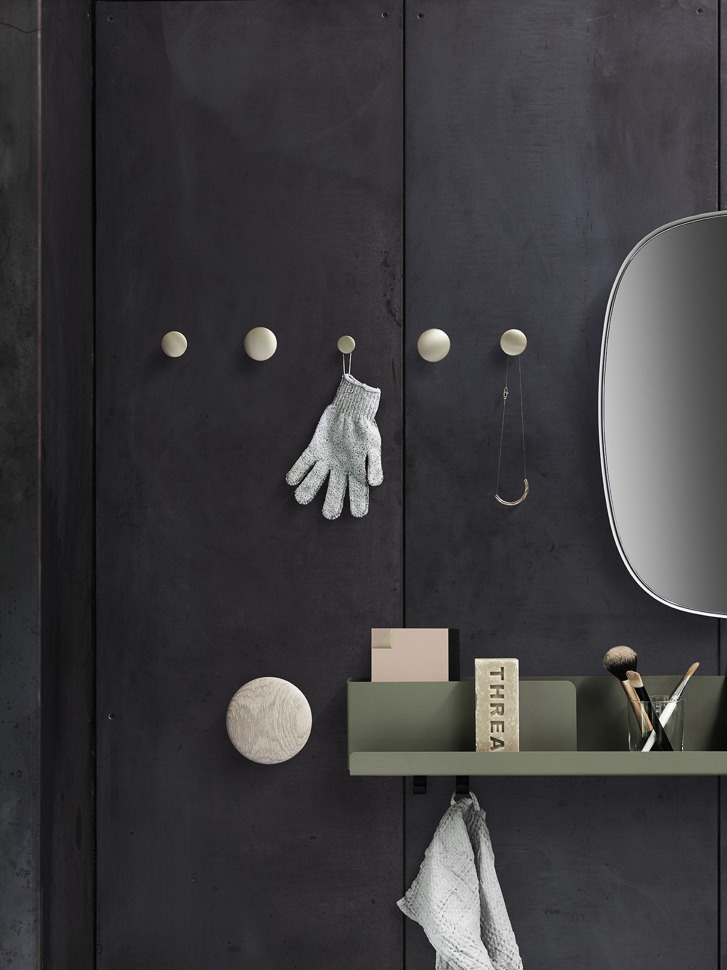 "Dark textured wall with brass hooks, green shelf, and a round mirror for a modern, minimalist aesthetic."