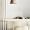 Minimalist wooden furniture in light tones, accented by earthy greens and a warm gold pendant light.