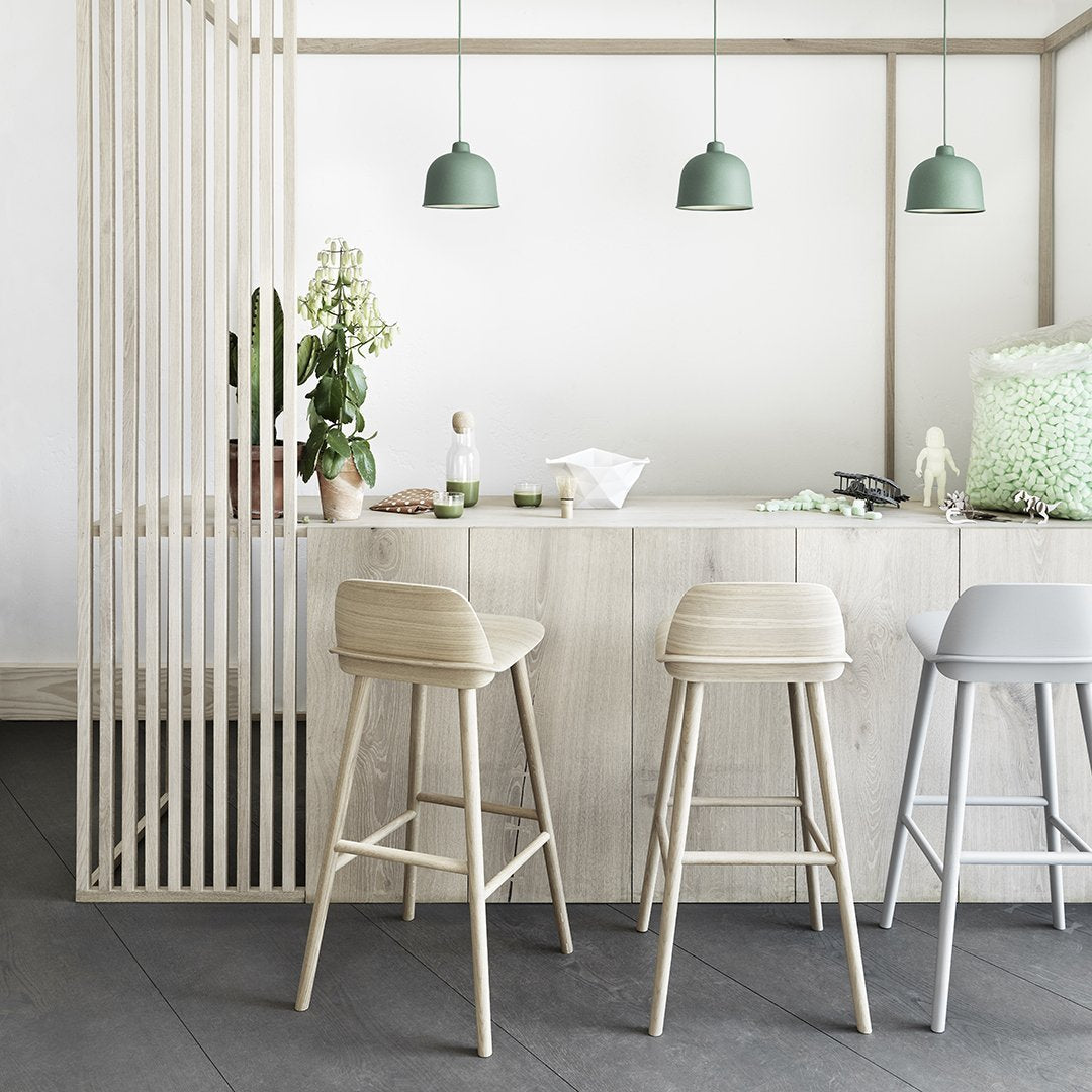 Light wood cabinetry, pale gray and beige bar stools, and green pendant lights create a fresh, modern aesthetic.