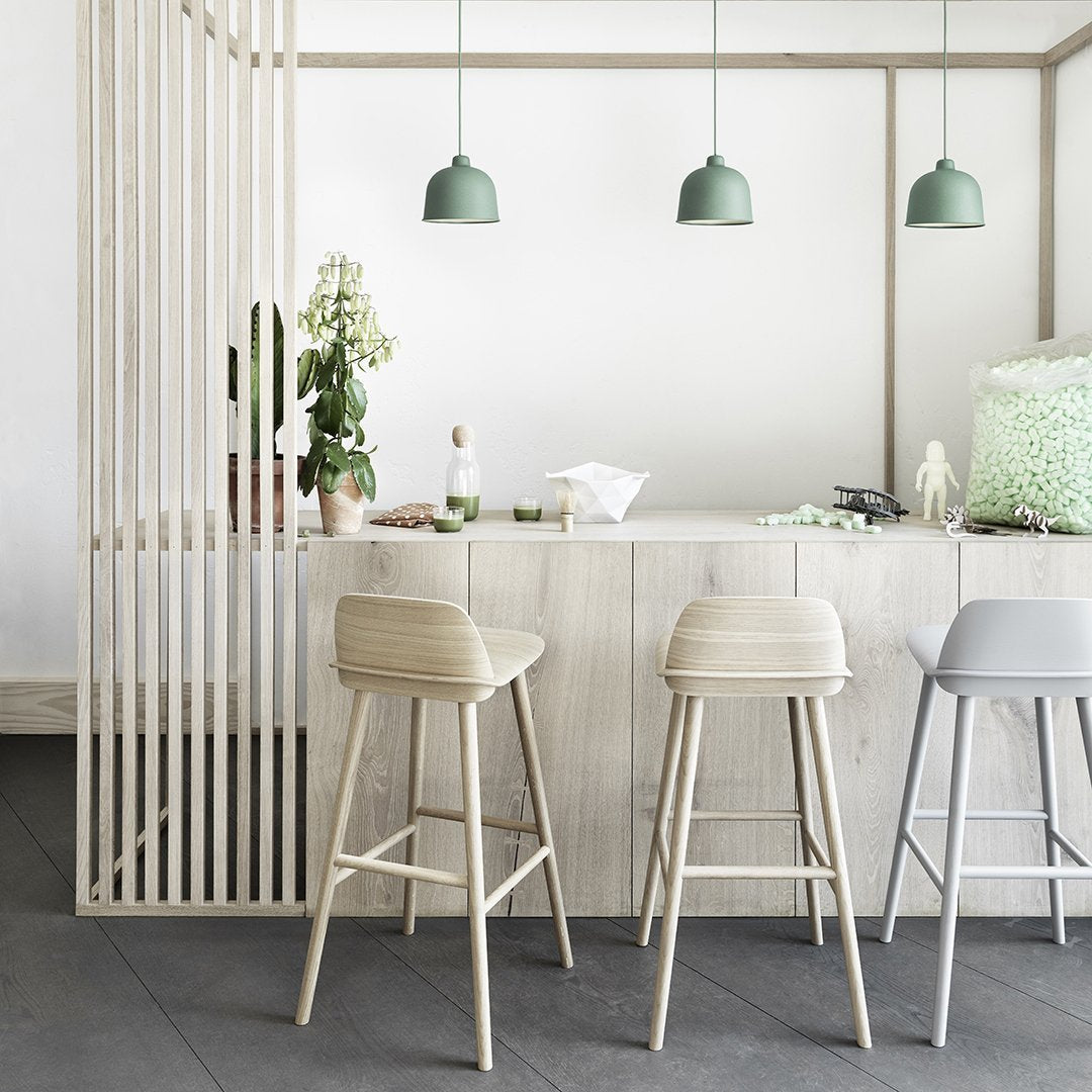Light wood bar with beige and gray stools, accented by green pendant lights and soft green decor. Clean, modern aesthetic.