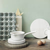 White cookware on textured white and gray surfaces, featuring subtle patterns and soft pastel green background.