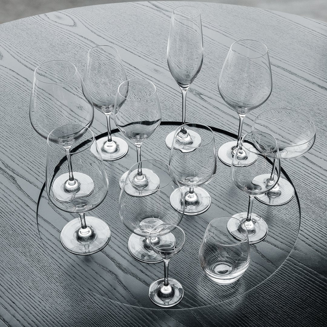 Set of crystal clear wine glasses with elegant shapes, displayed on a textured gray wooden surface.