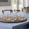 Set of clear glass tumblers on a round wooden tray, featuring fresh lime slices, against a light blue table.