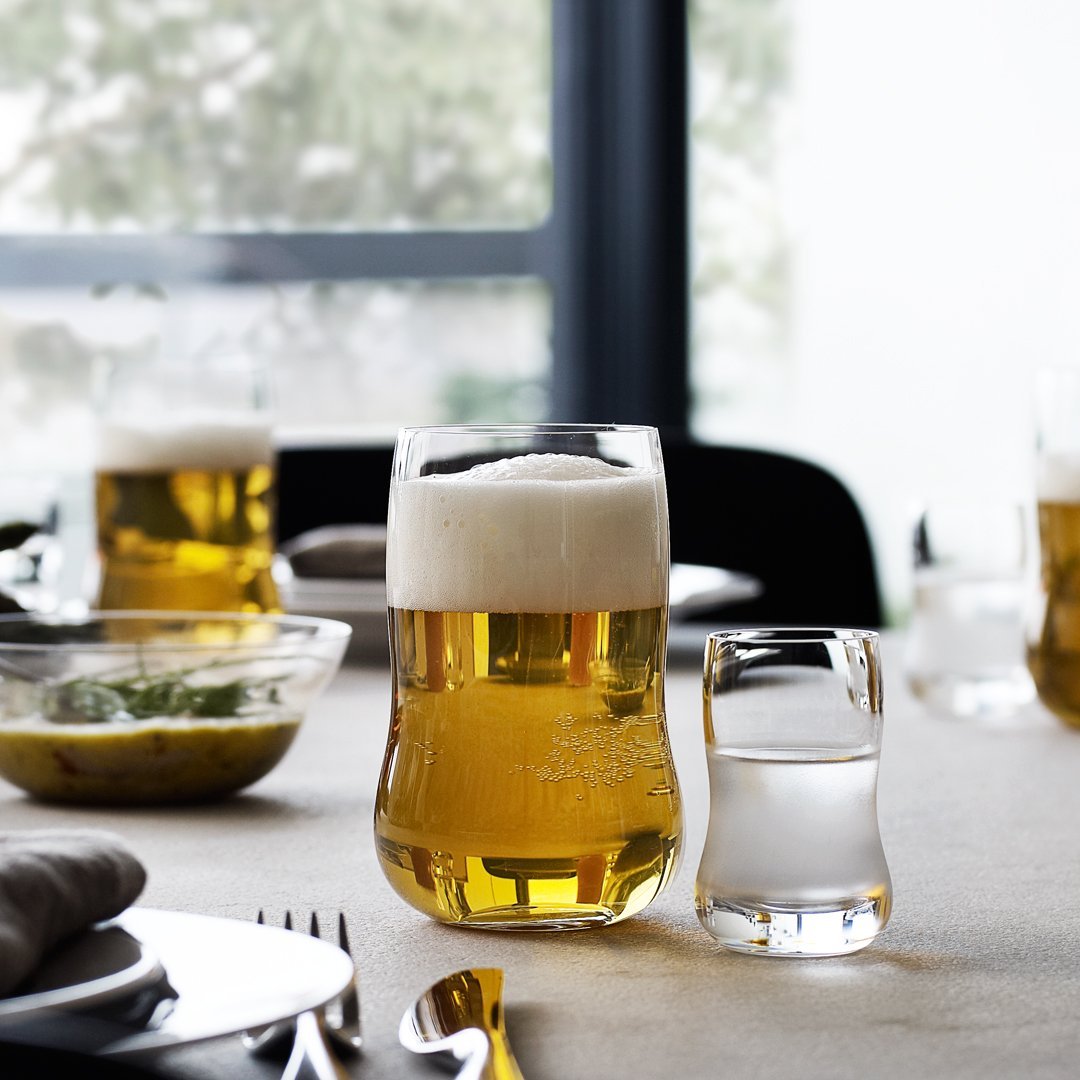 Clear glass beer and shot glasses filled with golden beer and colorless liquid, surrounded by a neutral table setting.