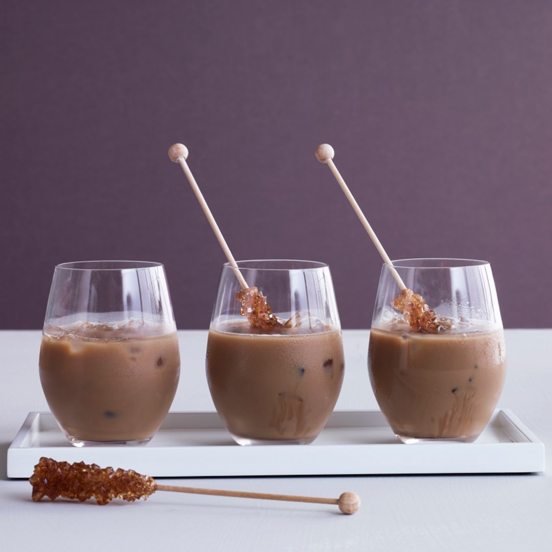 Three glasses of iced coffee with brown sugar sticks on a white tray, against a purple background.