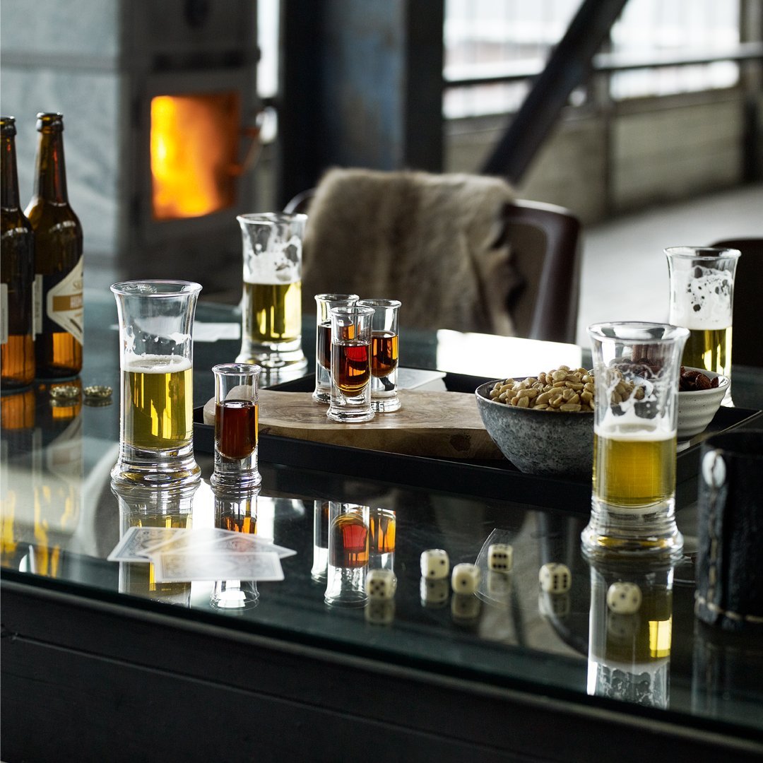 Beer glasses in clear glass featuring light gold and rich amber drinks, set against a reflective table and rustic background.