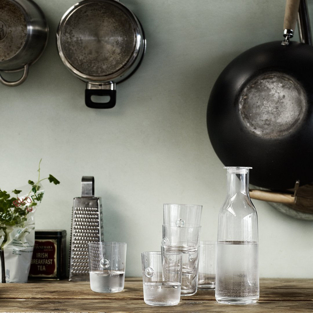 Clear glassware set on a wooden table, featuring varying heights and simple patterns, against a muted green backdrop.