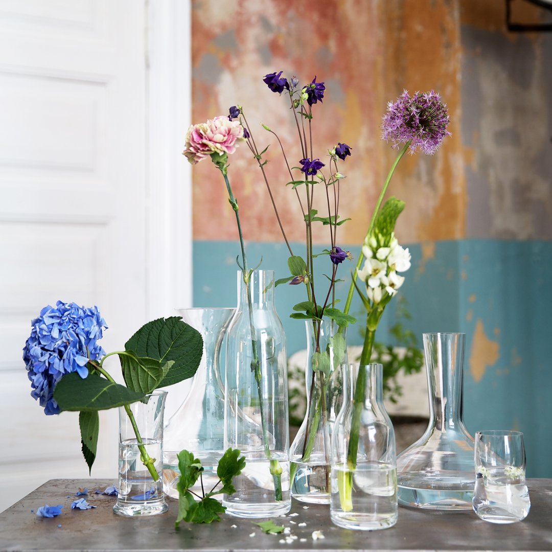 "Clear glass vases with pastel flowers against a textured blue and orange wall backdrop."