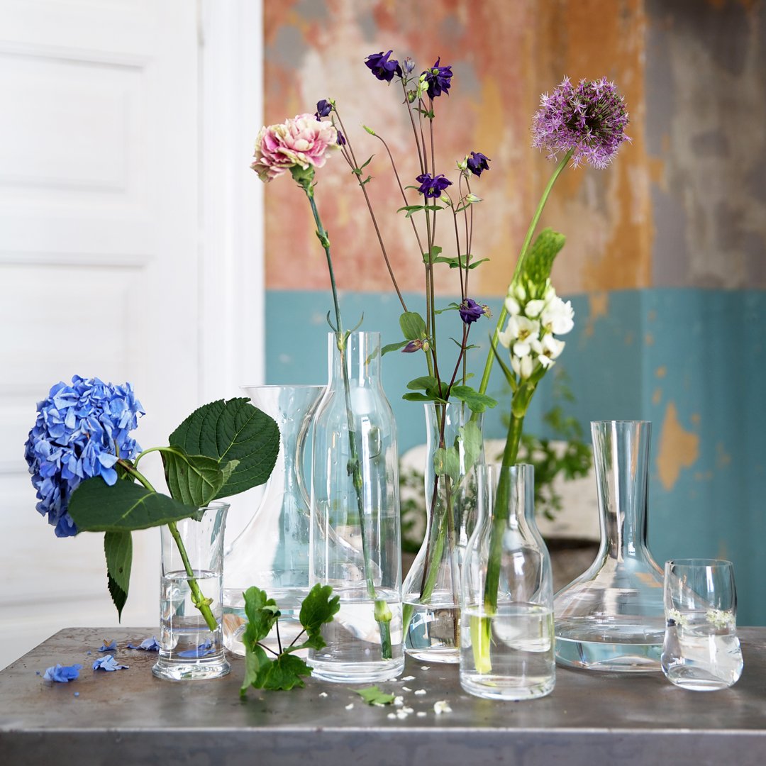 Clear glass vases with colorful flowers; vibrant blues, purples, and greens against a softly-coated backdrop.