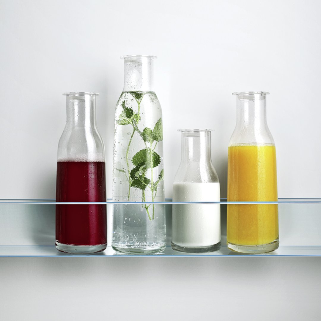 Four stylish glass bottles displaying vibrant hues: deep red, clear with green mint, creamy white, and bright yellow.
