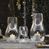 Set of three clear glass lanterns with light beige straps, featuring rounded shapes and soft candlelight glow.